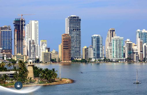 Vista panorámica de una moderna ciudad costera con rascacielos frente a una bahía tranquila. En primer plano destaca una pequeña península con abundante vegetación tropical y una histórica torre de piedra, creando un atractivo contraste entre patrimonio, naturaleza y desarrollo urbano bahía de boca grande Tour de un día en yate por Cartagena: itinerarios recomendados navega colombia
